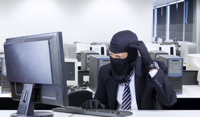 Een man in kostuum met een bivakmuts zit achter een computerscherm