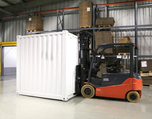 White container moved by forklift in storage space.