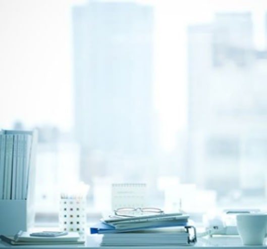 Close-up of a desk filled with office supplies, behind a window overlooking tall buildings