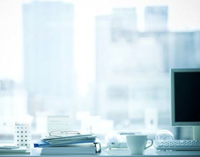 Close-up of a desk filled with office supplies, behind a window overlooking tall buildings