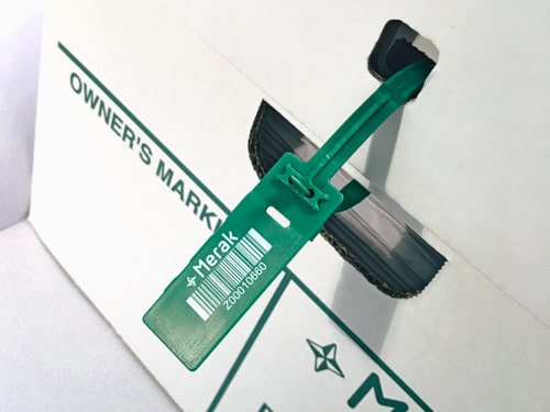 Green plastic seal with white bar code attached to the lid of a box